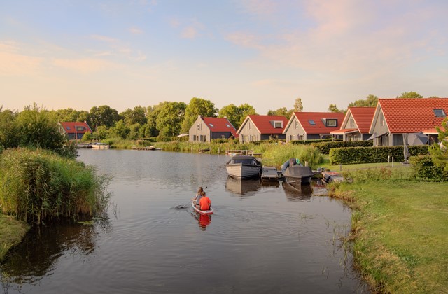 Mensen varen in een bootje langs vakantiewoningen