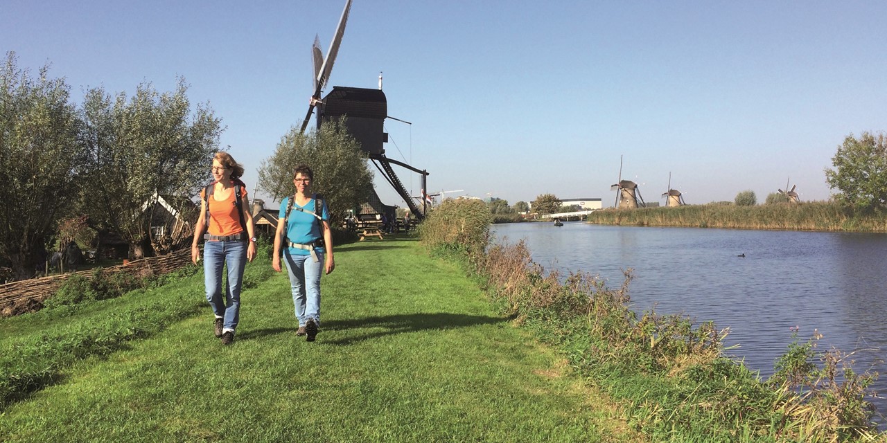 Duo wandelend langs het water met een molen op de achtergrond
