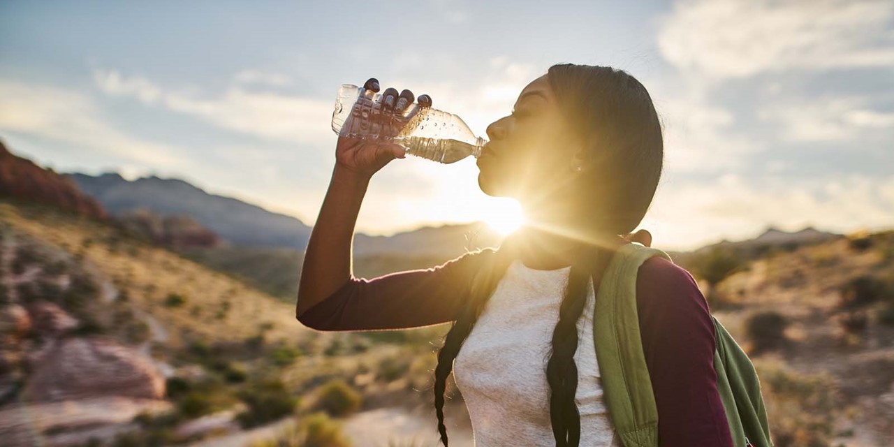 foto van een vrouw die uit een flesje drinkt in de zon.