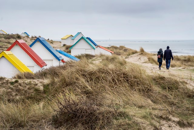 wandelaars in de duinen van Cotentin, bij kleurrijke huisjes.